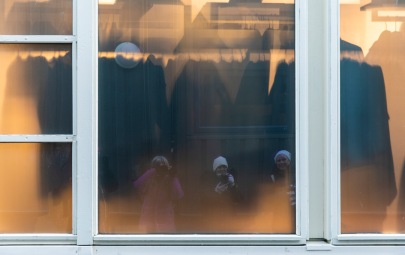Foto: Eli Kristin Hårberg | Tittel: På utstilling | Sted: Gaubekveita | Tre fotovenner speiles i ruta. Synes fargene i bildet ble fine. Den gule ruta skjuler delvis hva som er på innsiden… vi kan anta at det muligens er et kleslager.